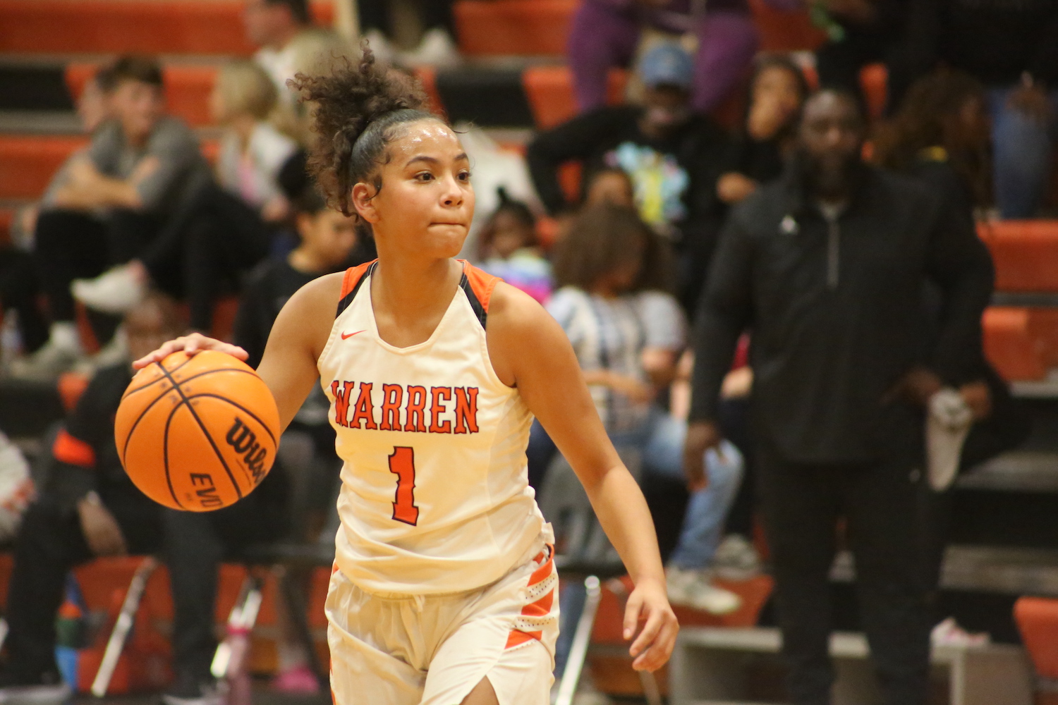 A girl in white and orange basketball uniform holding a ball.