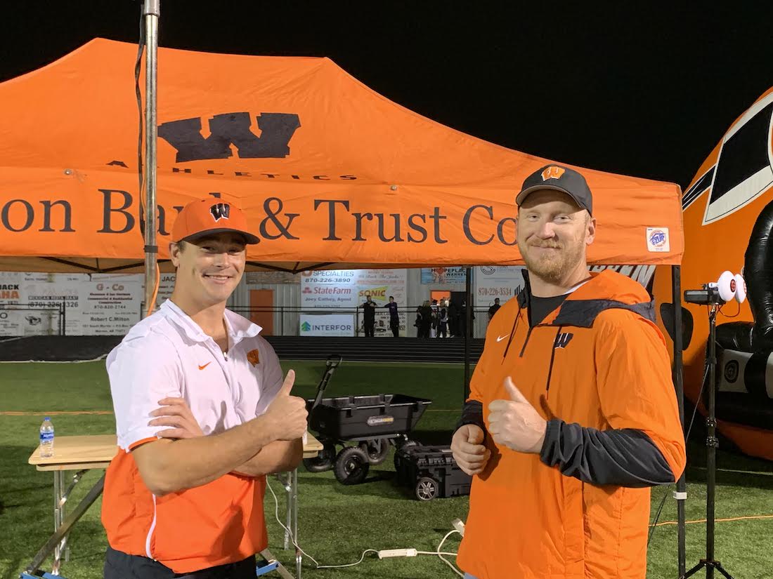 Two men in orange jackets giving thumbs up.