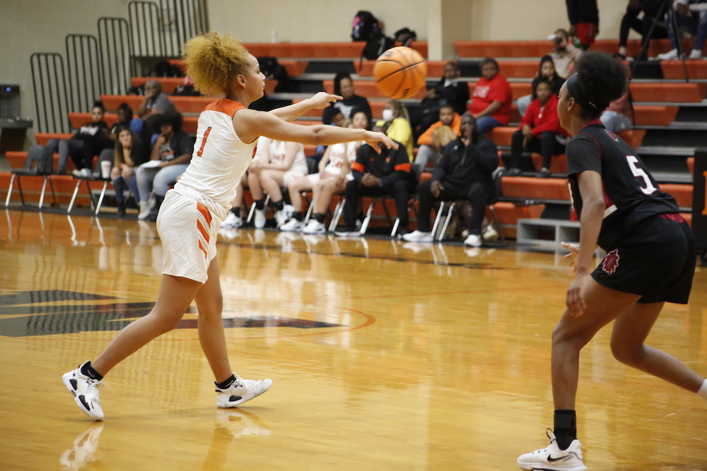 A girl in white and orange uniform holding a basketball.