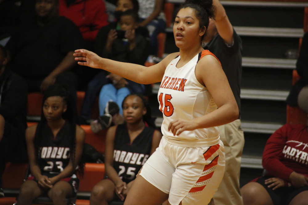 A girl in white and orange basketball uniform playing basketball.