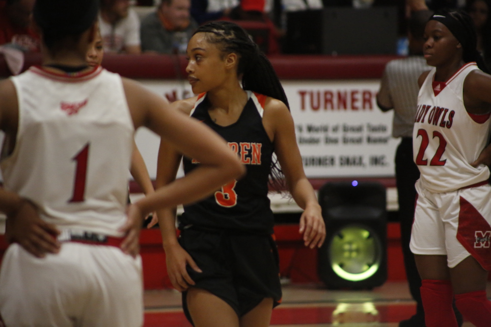A girl in black and white basketball uniform playing basketball.