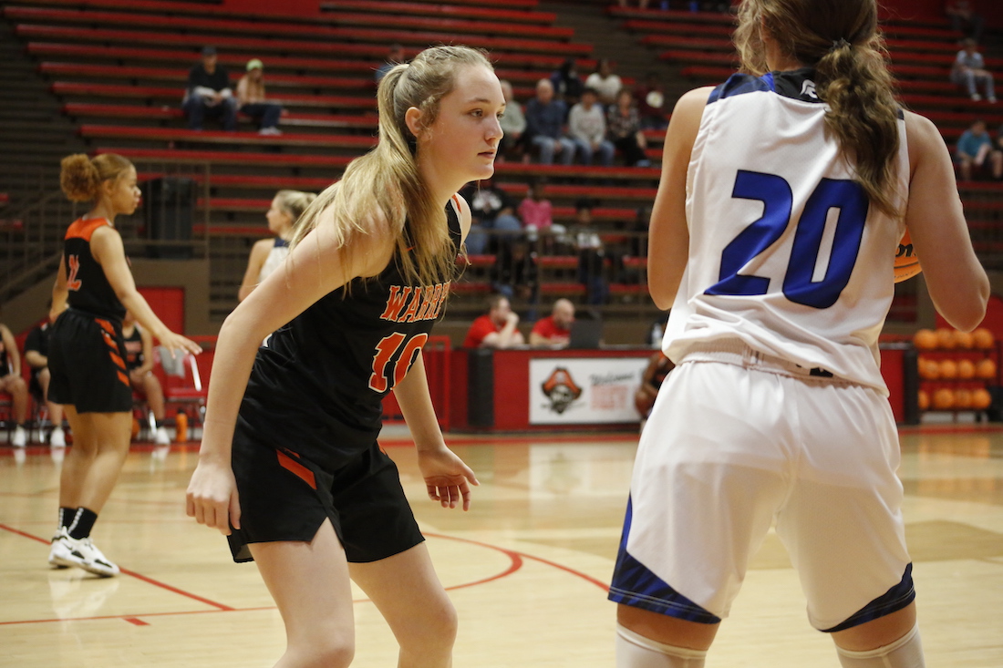 A girl in black and orange basketball uniform playing basketball.