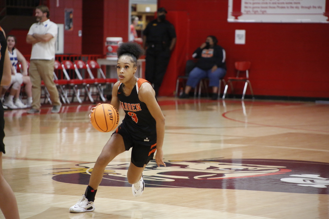A young person dribbles the basketball on a court.