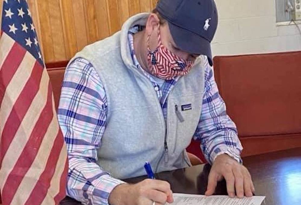 A man wearing a face mask writing on paper.