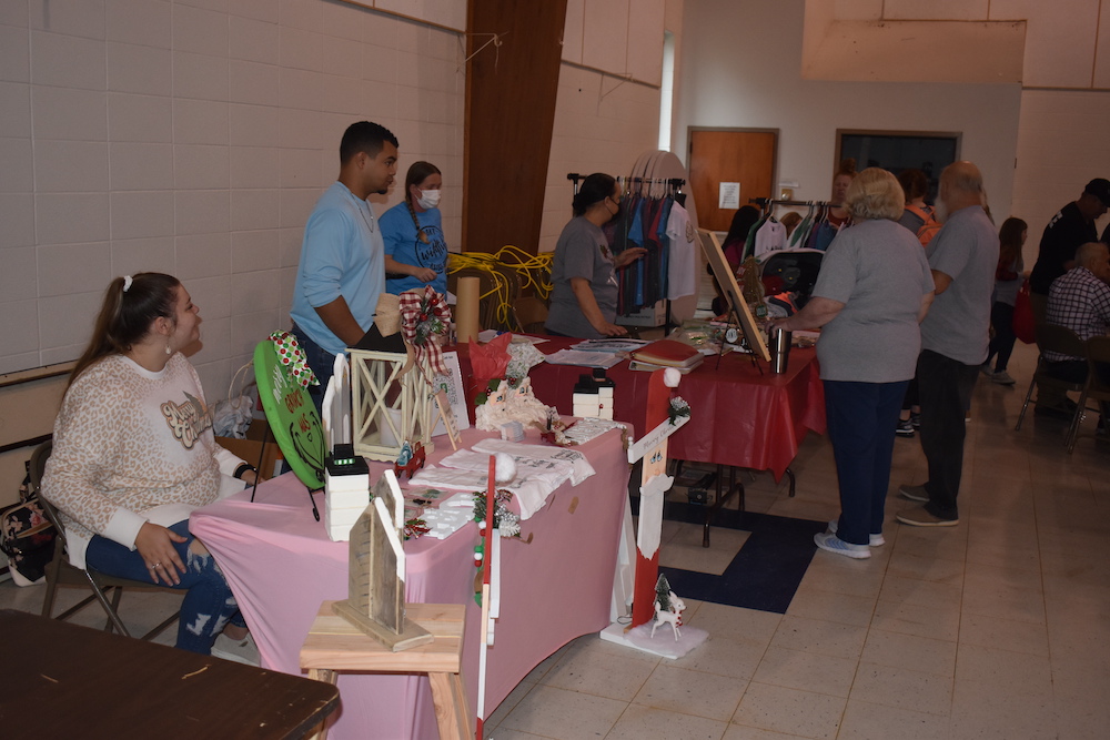 A group of people standing around tables with items.