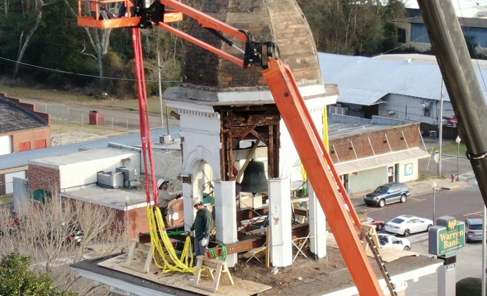 A crane is being used to lift the bell from the top of a building.