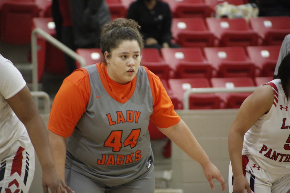 A woman in an orange and gray uniform is playing basketball.