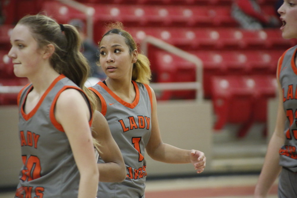 Two women in grey and orange uniforms are playing basketball.