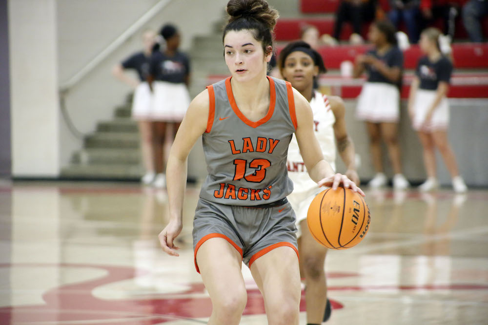 A girl in grey and orange basketball uniform holding a ball.
