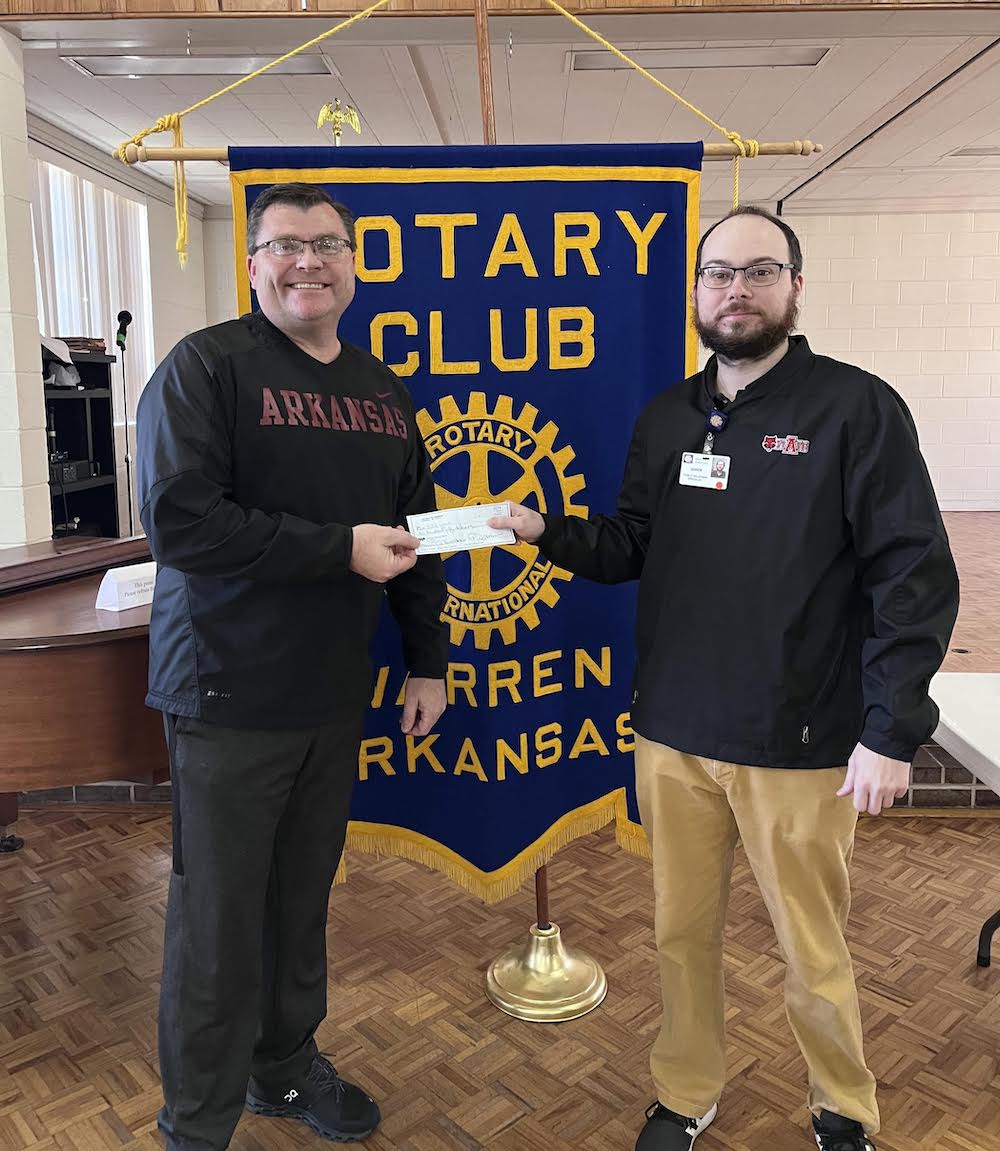 Two men holding a white box in front of a rotary banner.