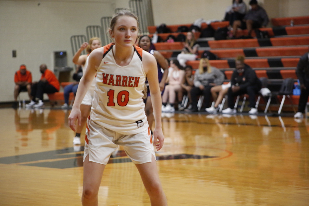 A girl in white and orange basketball uniform playing basketball.