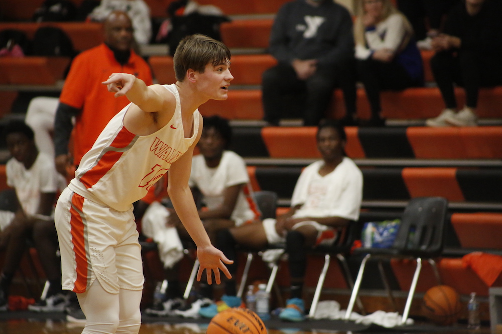 A boy in white shirt playing basketball on court.