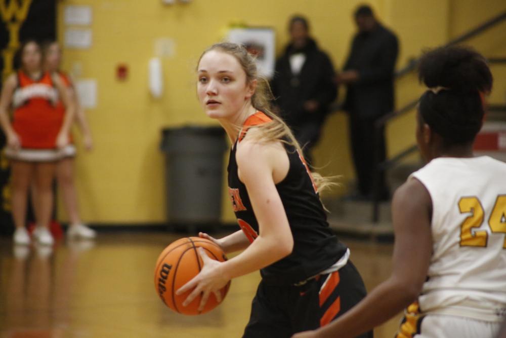 A girl in black and orange basketball uniform holding a ball.