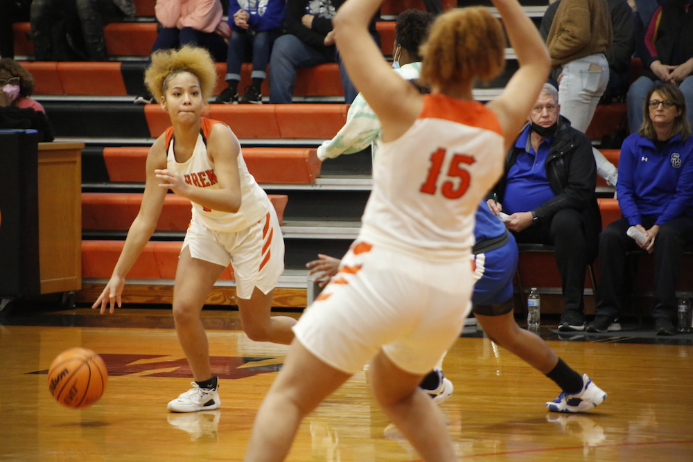 Two women playing basketball on a court with people watching.