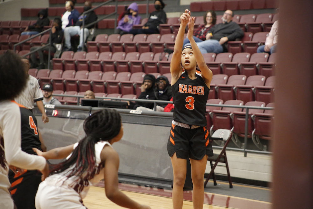 A girl in black and orange basketball uniform holding up her hands.