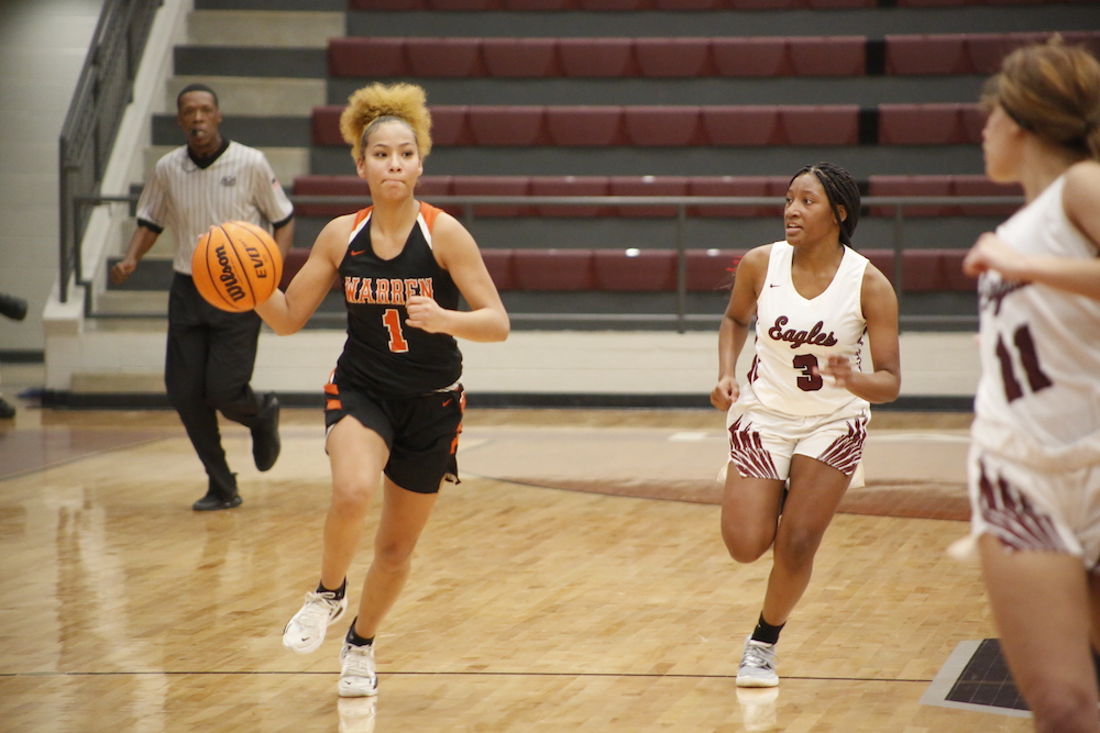 A girl in black and orange basketball uniform holding a ball.