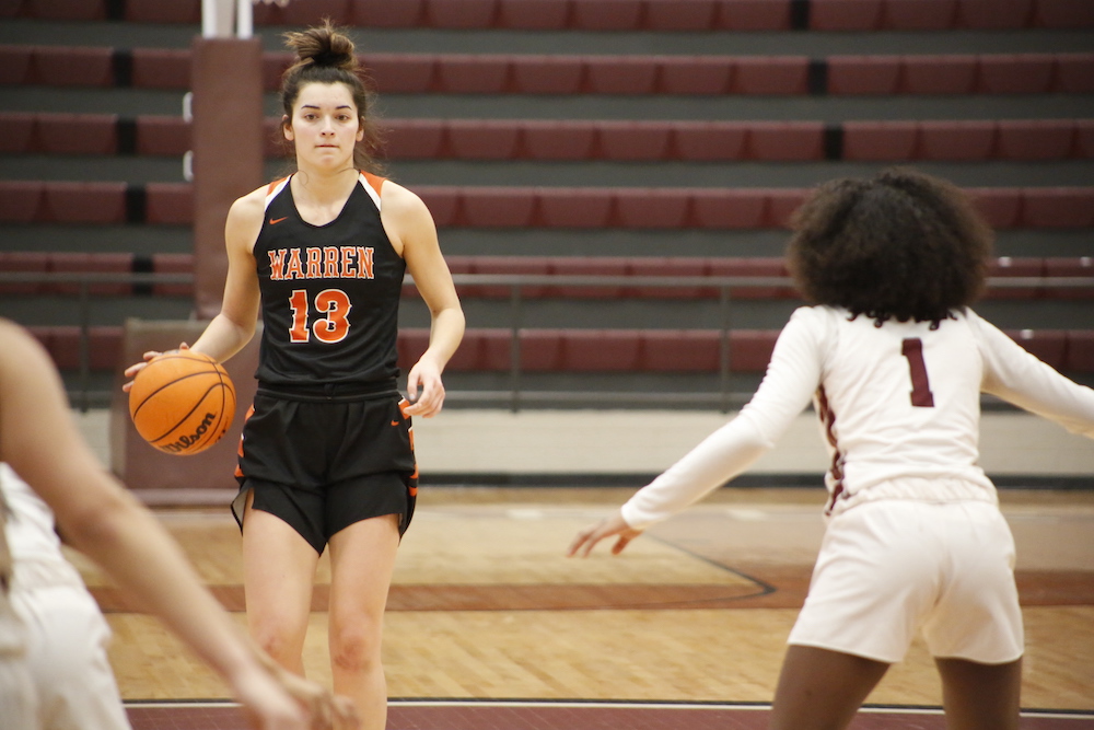 A girl in black and orange basketball uniform playing basketball.