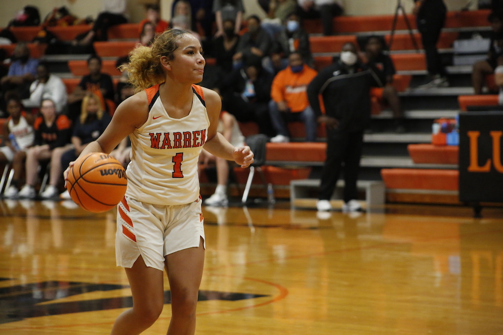 A girl in white and orange basketball uniform holding a ball.