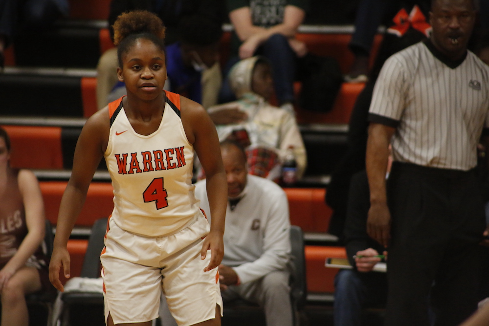 A woman in white and red basketball uniform playing basketball.
