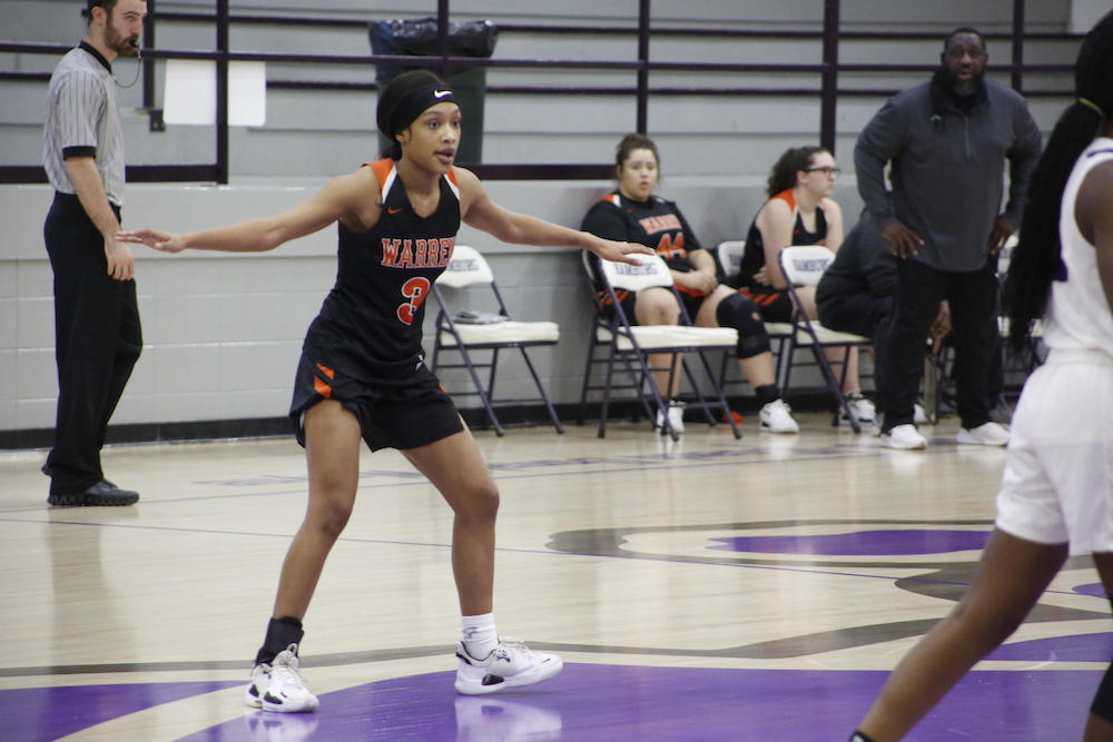 A girl in black and orange basketball uniform playing basketball.