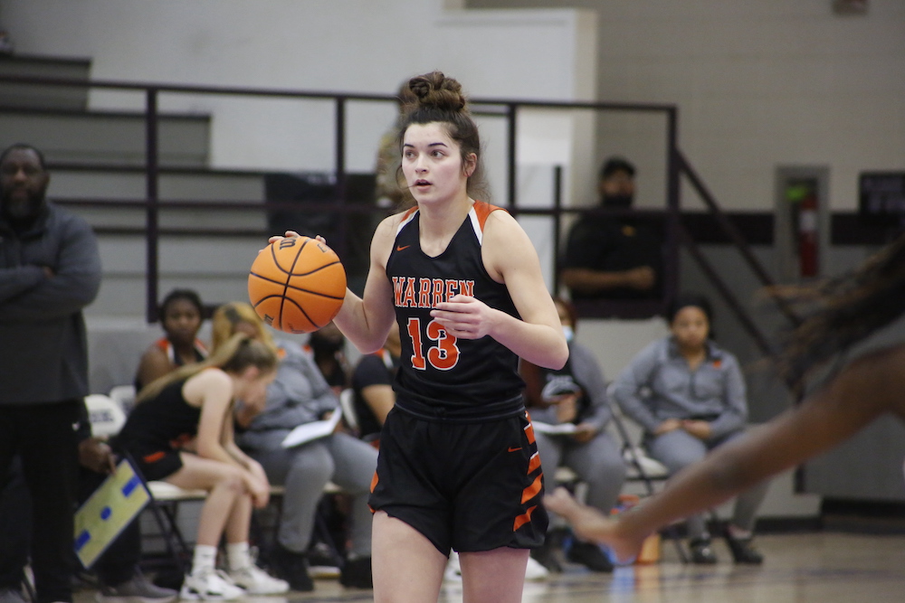 A girl in black and orange basketball uniform holding a ball.