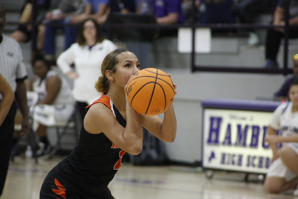 A girl is holding onto the basketball and aiming for it.