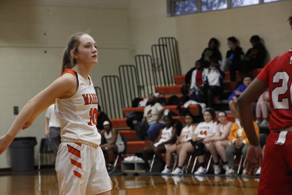 A girl in white and orange basketball uniform playing basketball.
