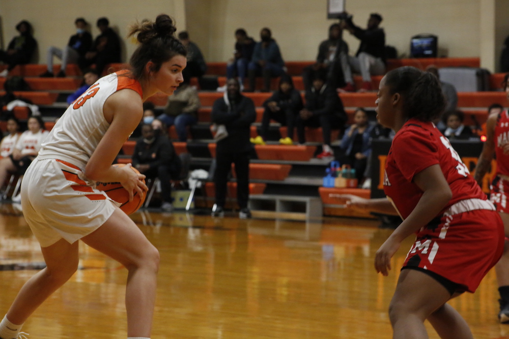 A girl in orange and white playing basketball.