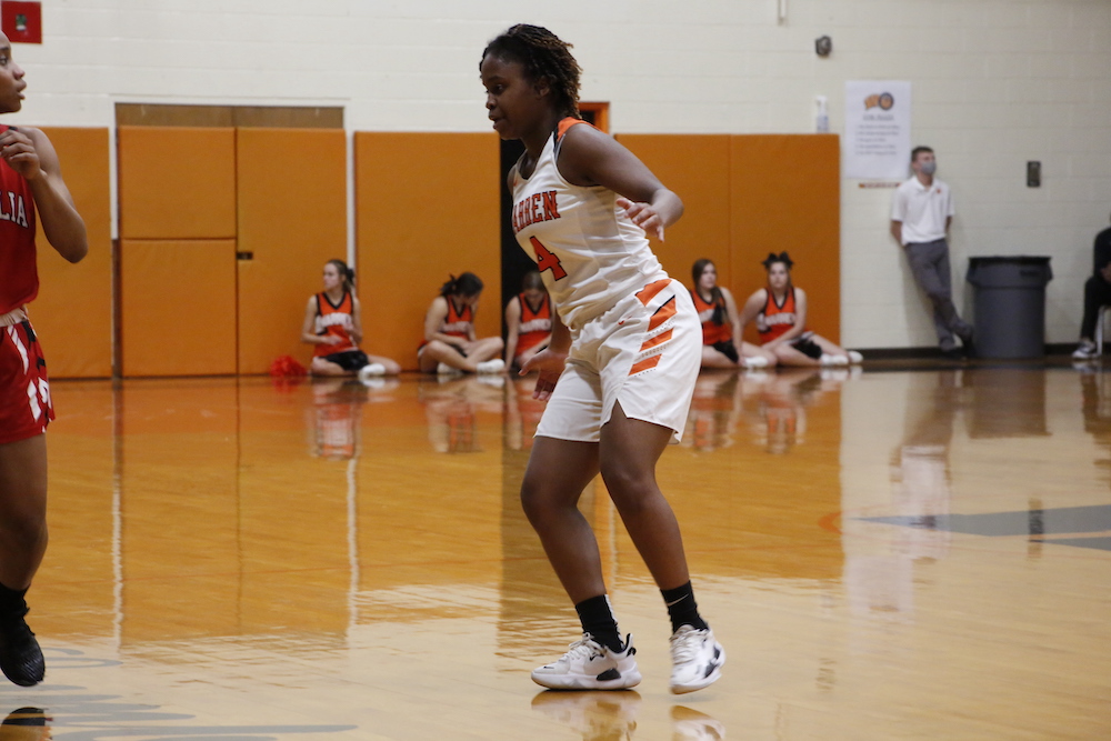 A girl in white and orange basketball uniform playing on the court.
