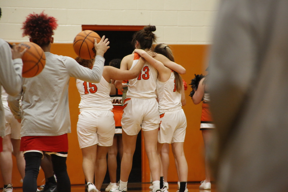 A group of girls standing next to each other holding onto a basketball.