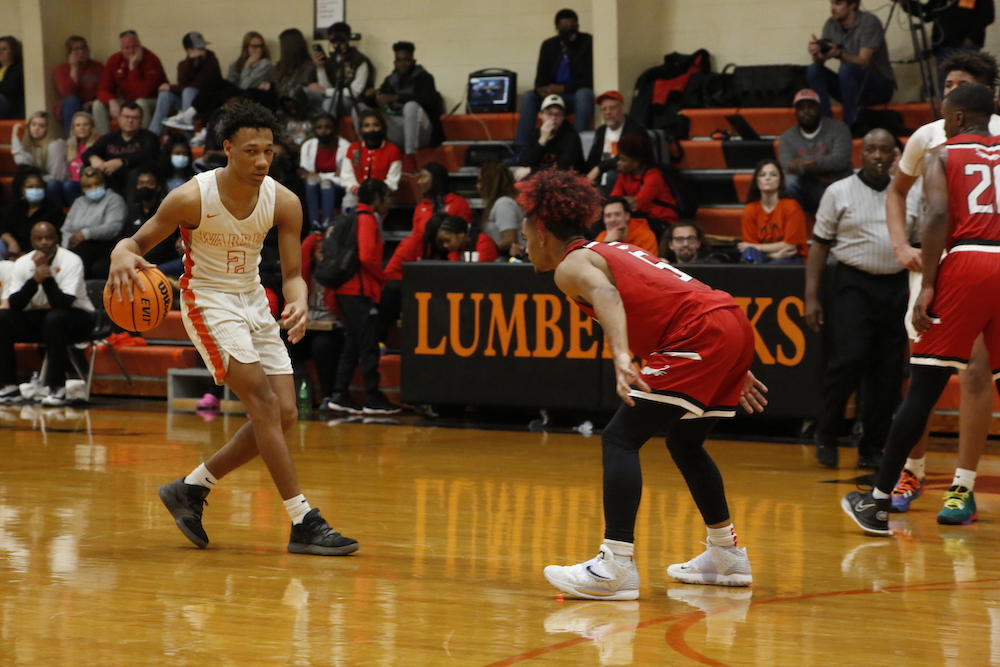 Two men playing basketball on a court with people watching.