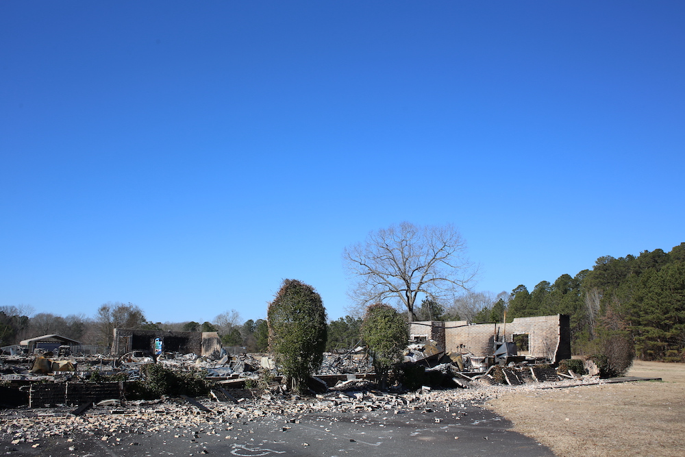 A fire destroyed house with trees and rubble in the foreground.