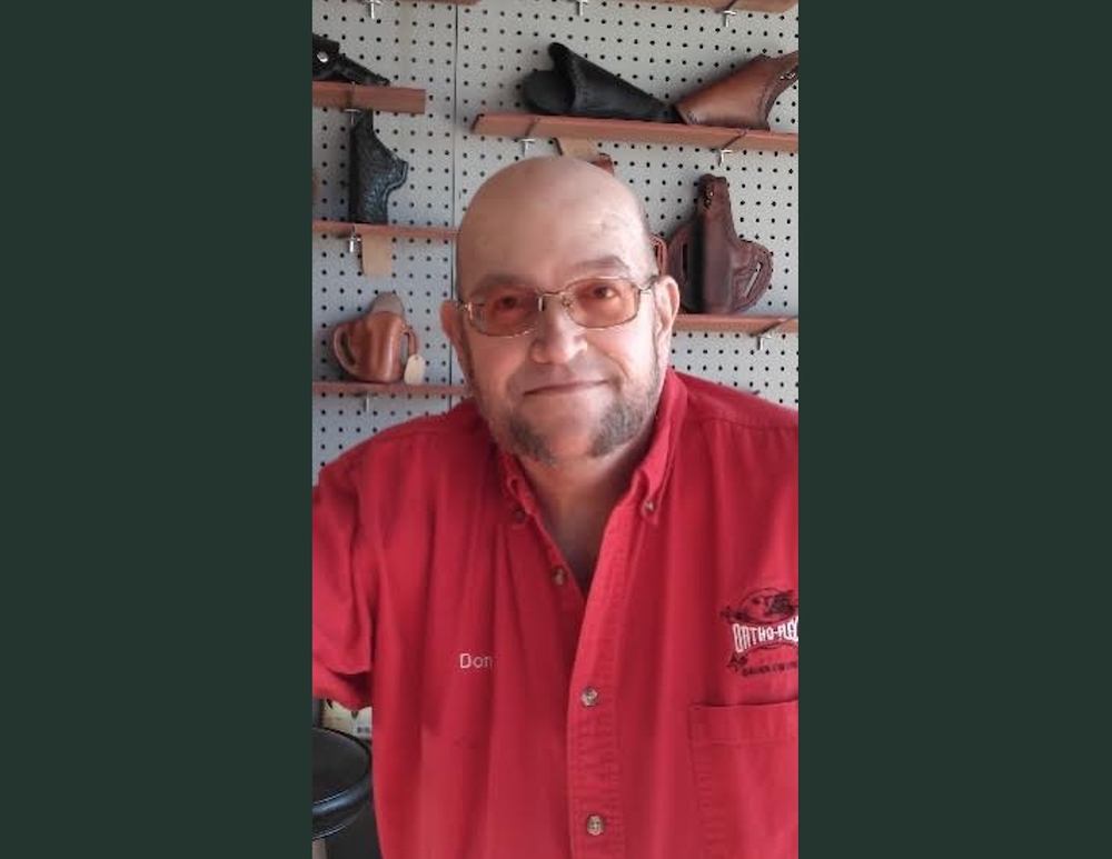 A man in red shirt and glasses standing next to wall.