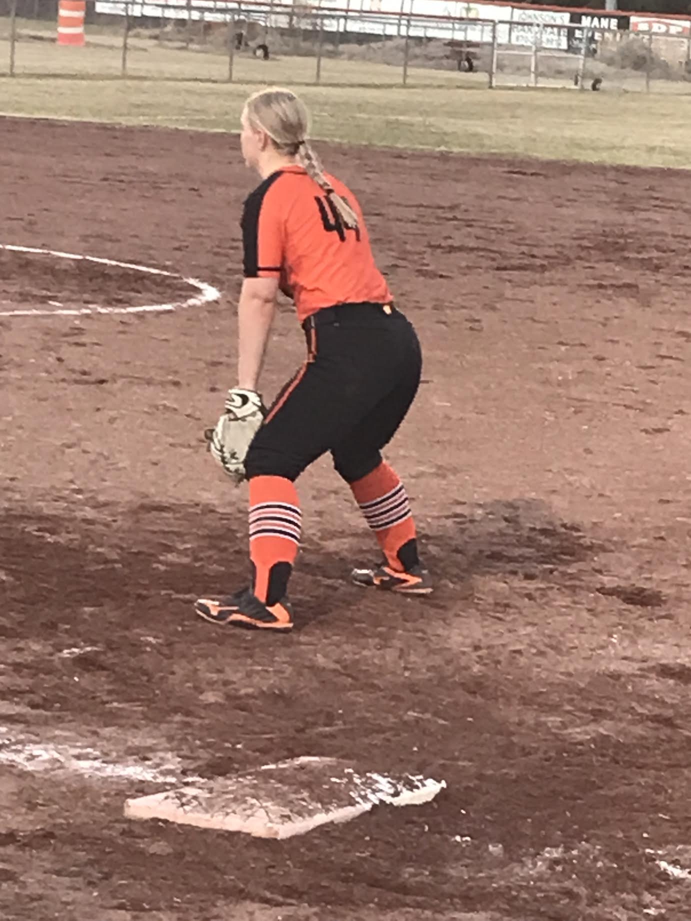 A girl in orange and black uniform holding a baseball bat.