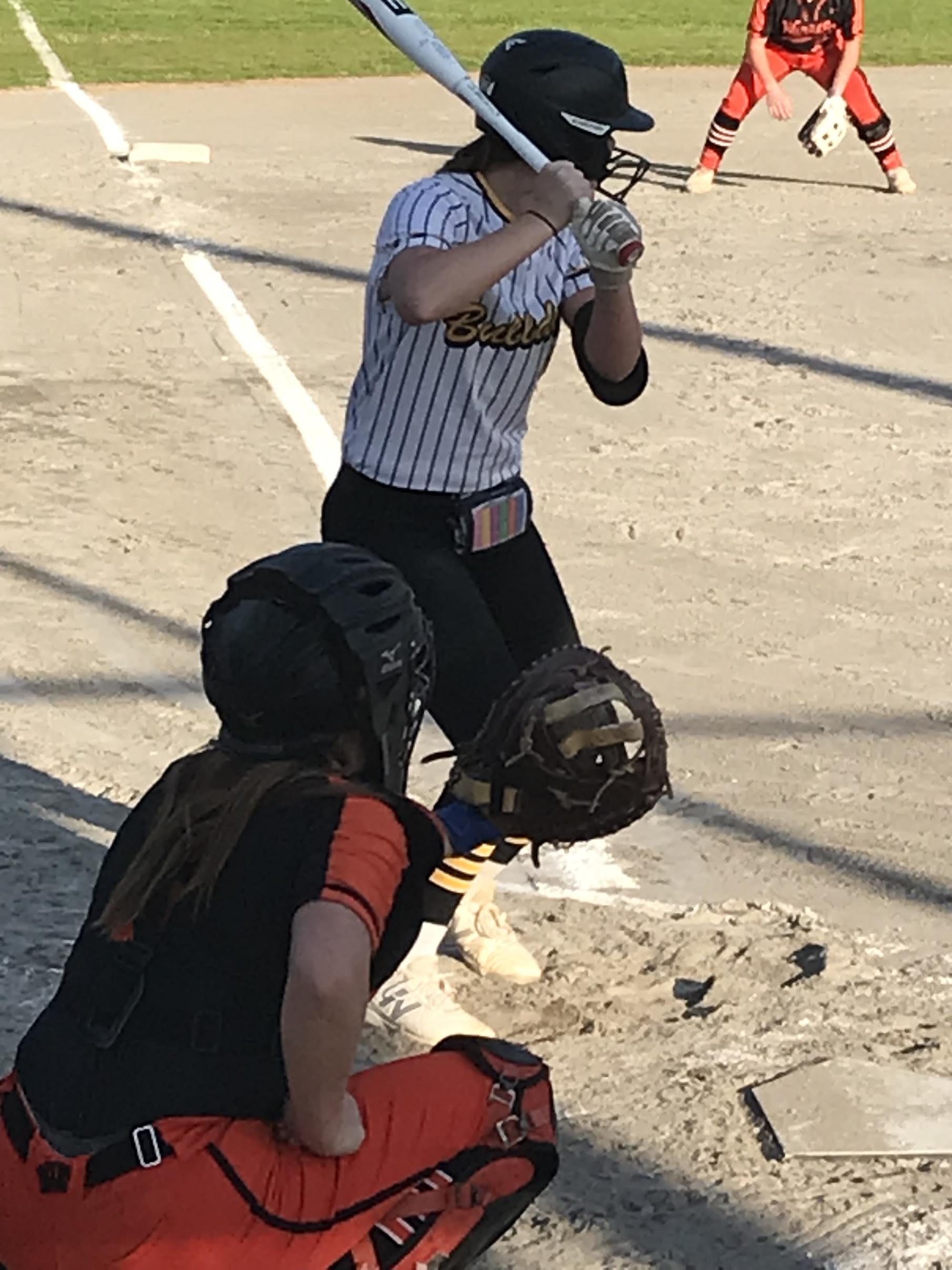 A girl in orange and black uniform holding a baseball bat.