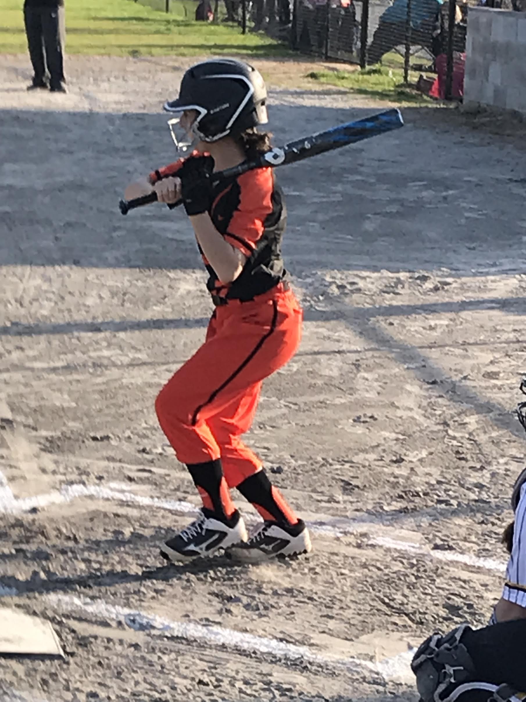 A girl in orange and black uniform holding a baseball bat.