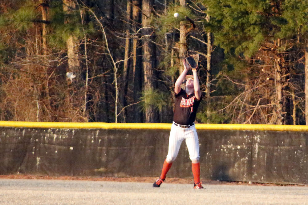 A girl in orange and black uniform holding a baseball bat.