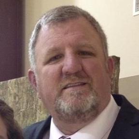 A man with grey hair and beard wearing a suit.