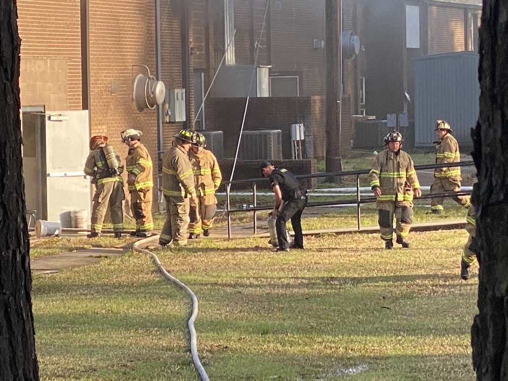 A group of firefighters standing around in the grass.