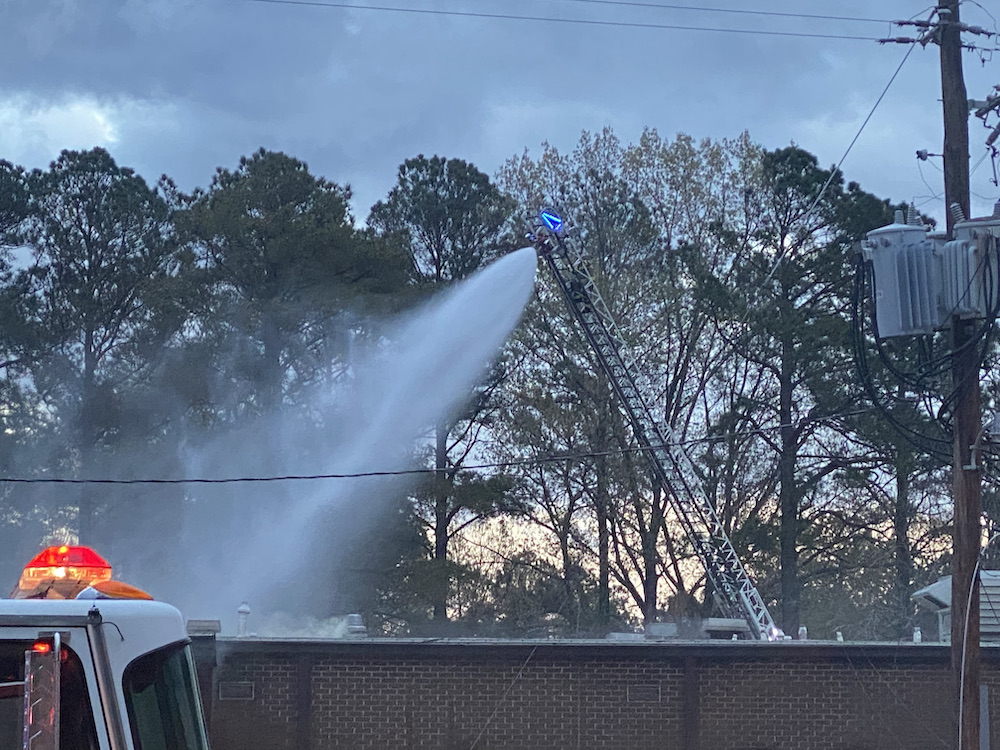 A fire truck is spraying water on the roof of a building.