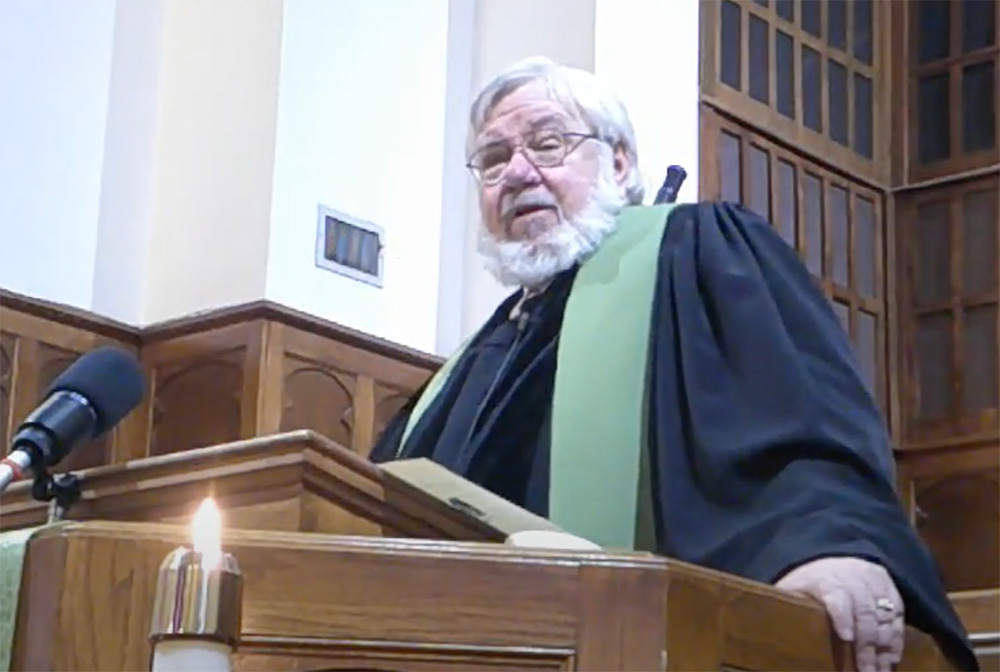 A man in a robe and green sash is holding a book.