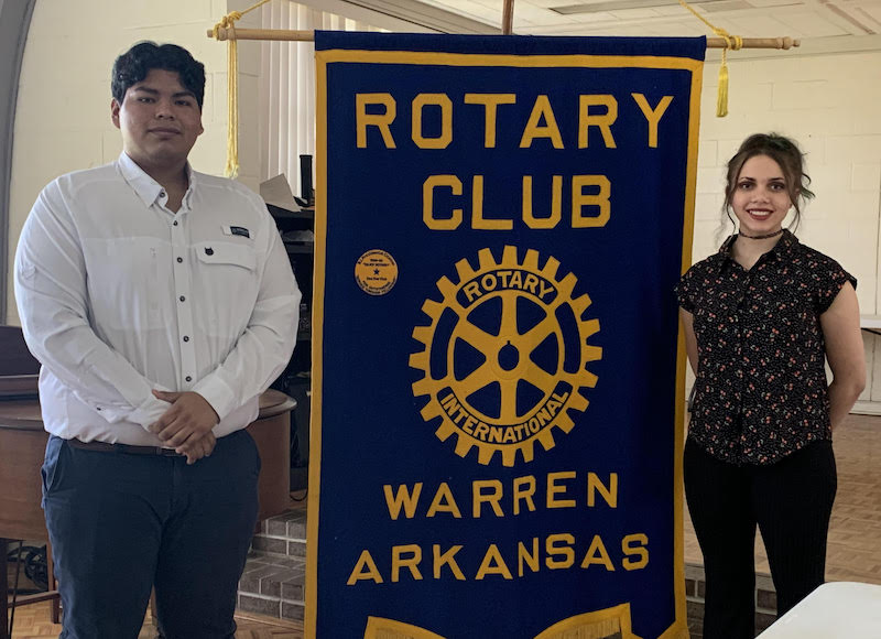 Two people standing next to a banner that says rotary club warren arkansas.