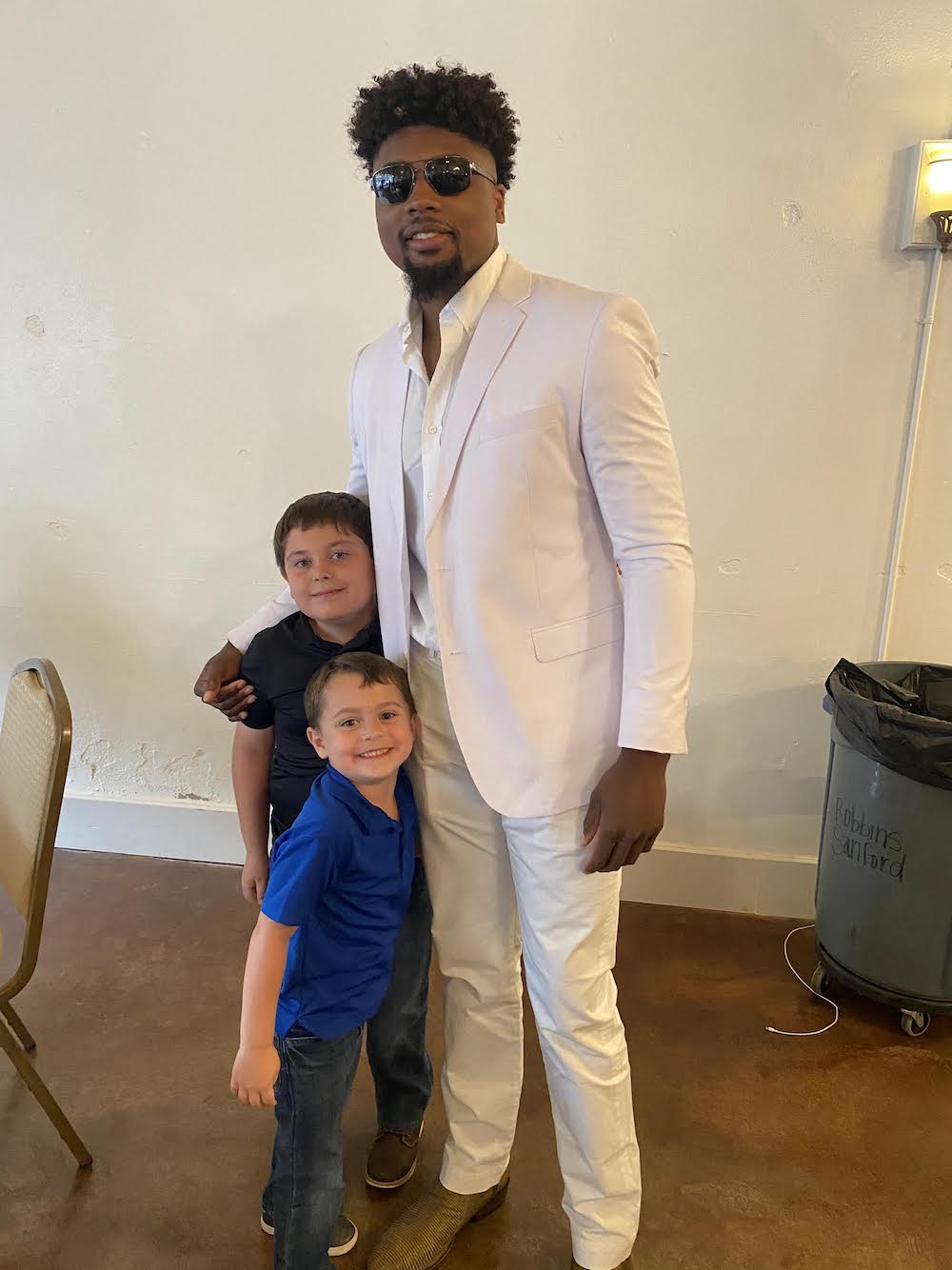 A man in white suit standing next to two boys.