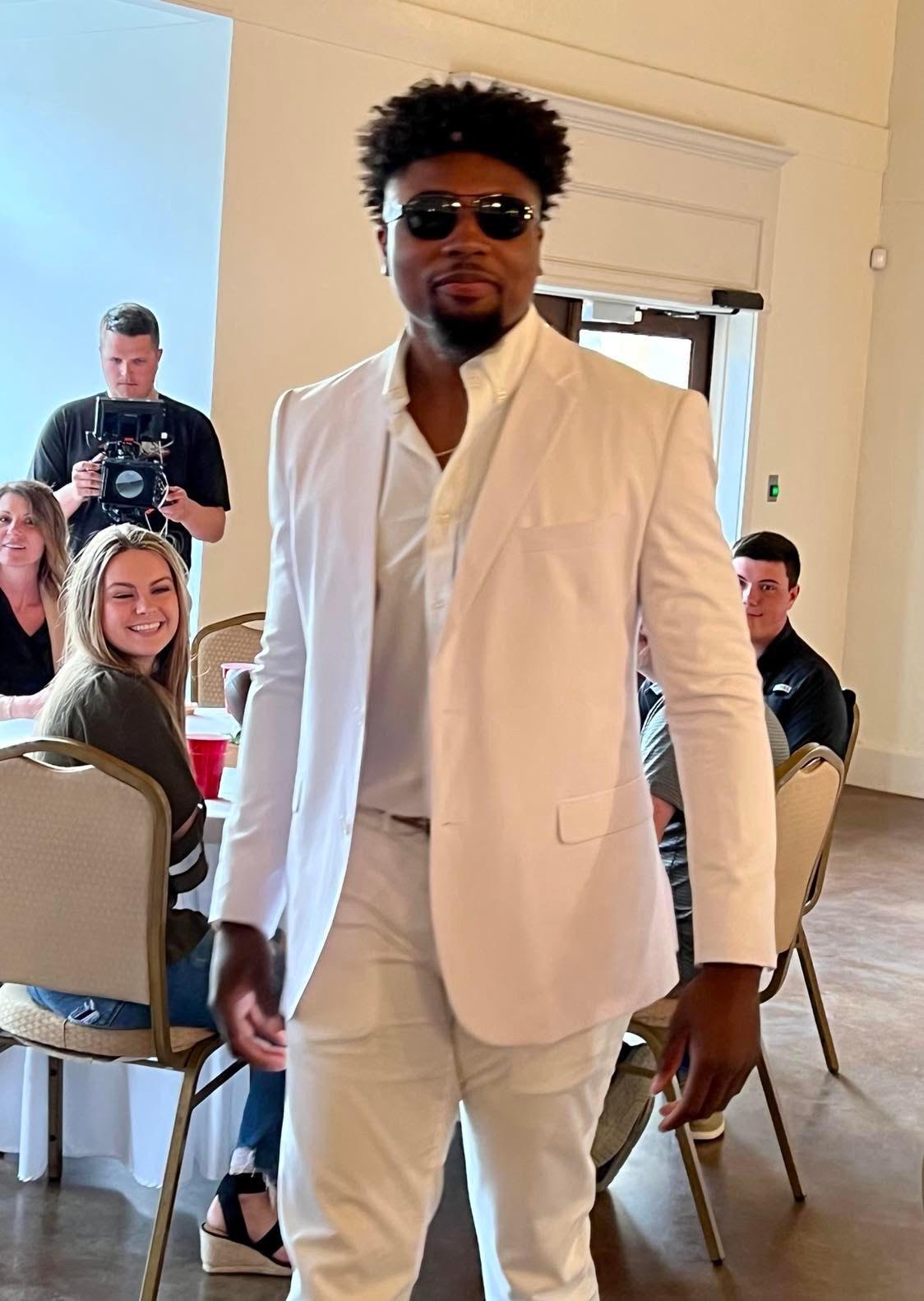 A man in white suit standing next to people.