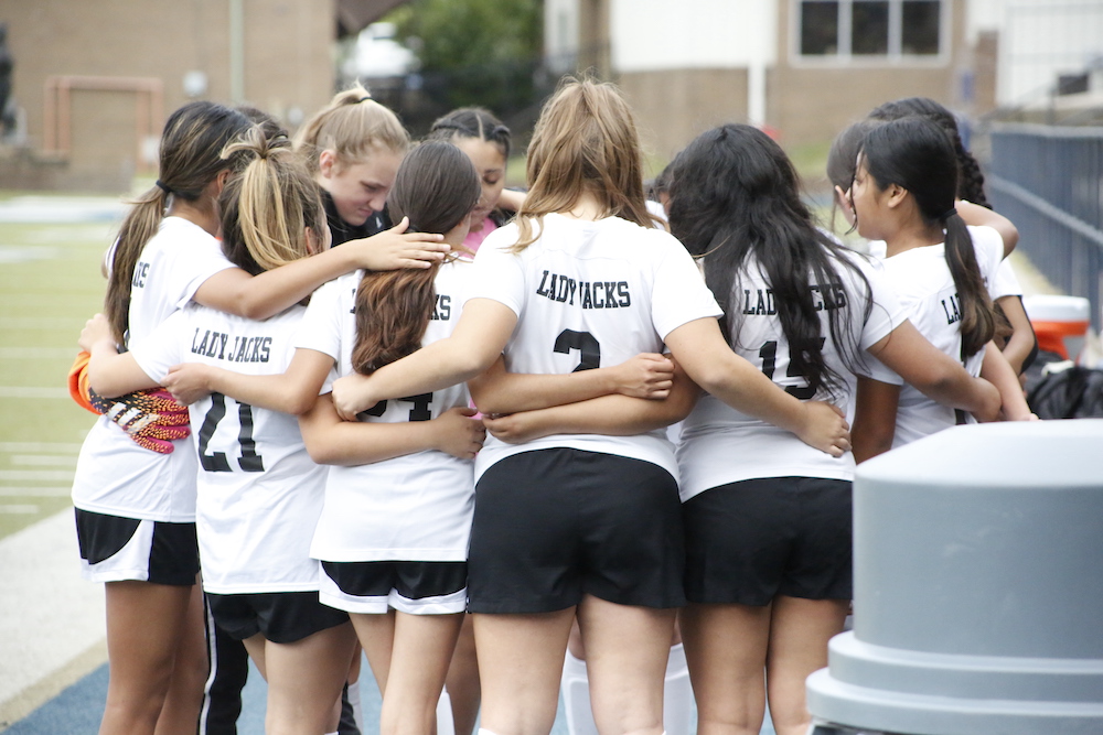 A group of girls huddle together in the middle of a soccer team.