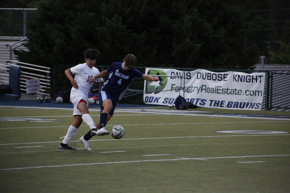 Two men playing soccer on a field with trees in the background.