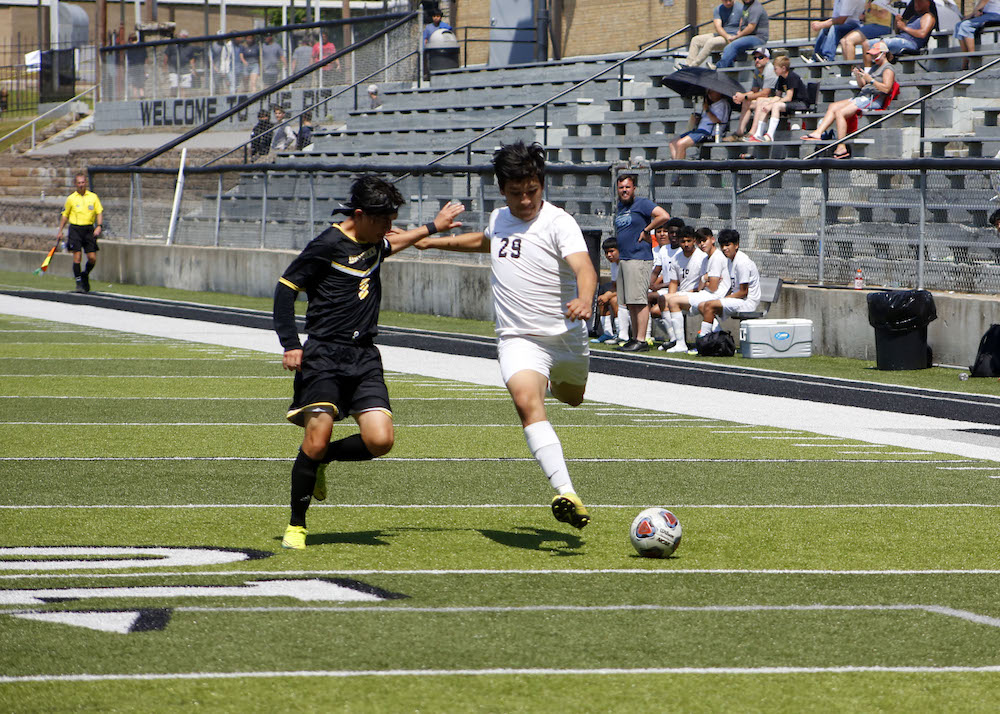 Two men playing soccer on a field with spectators watching.