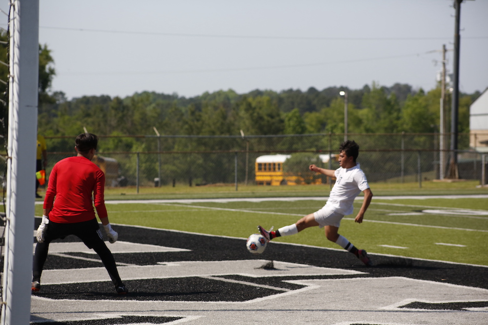 Two men playing soccer on a field with school buses in the background.