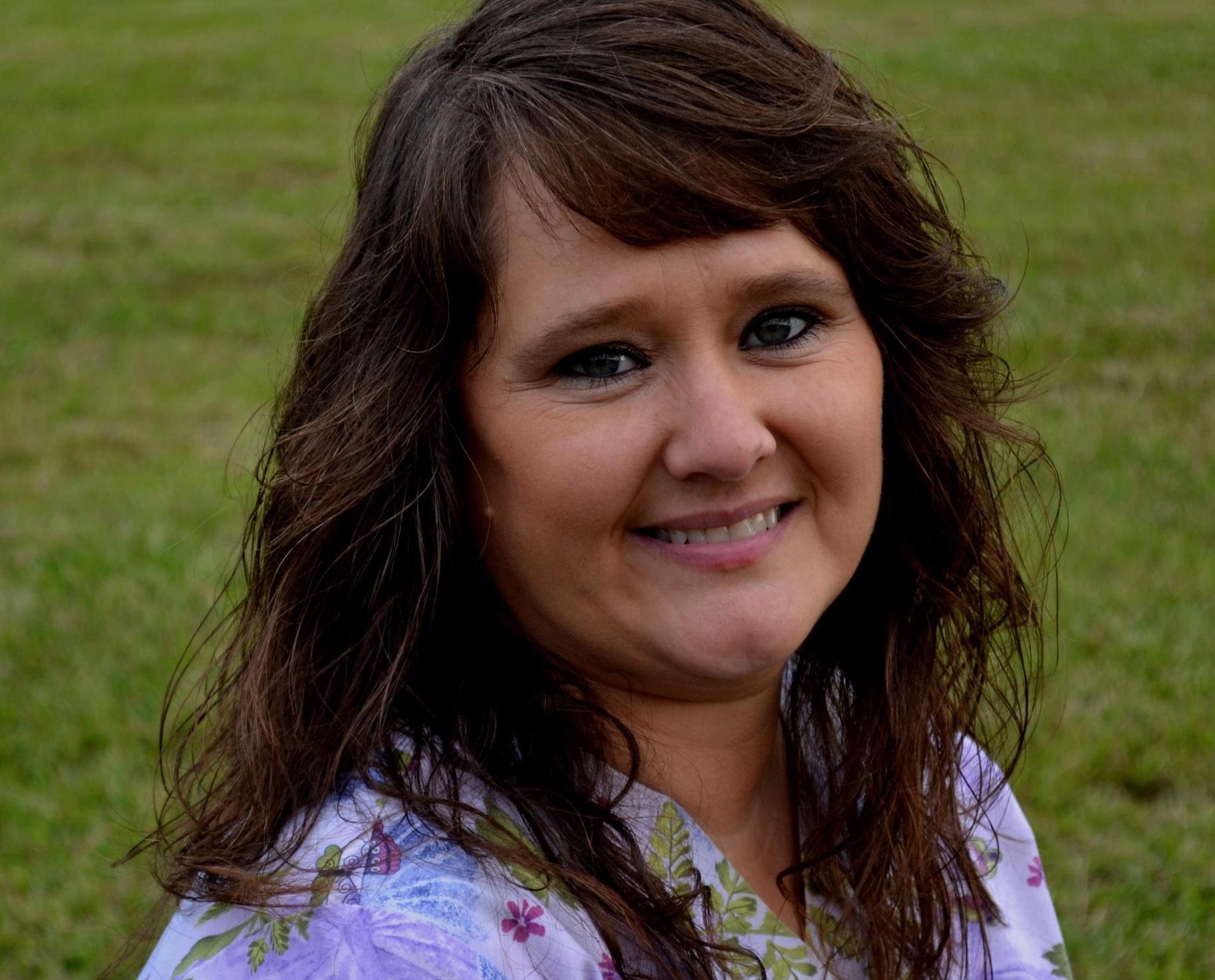 A woman with long brown hair standing in the grass.
