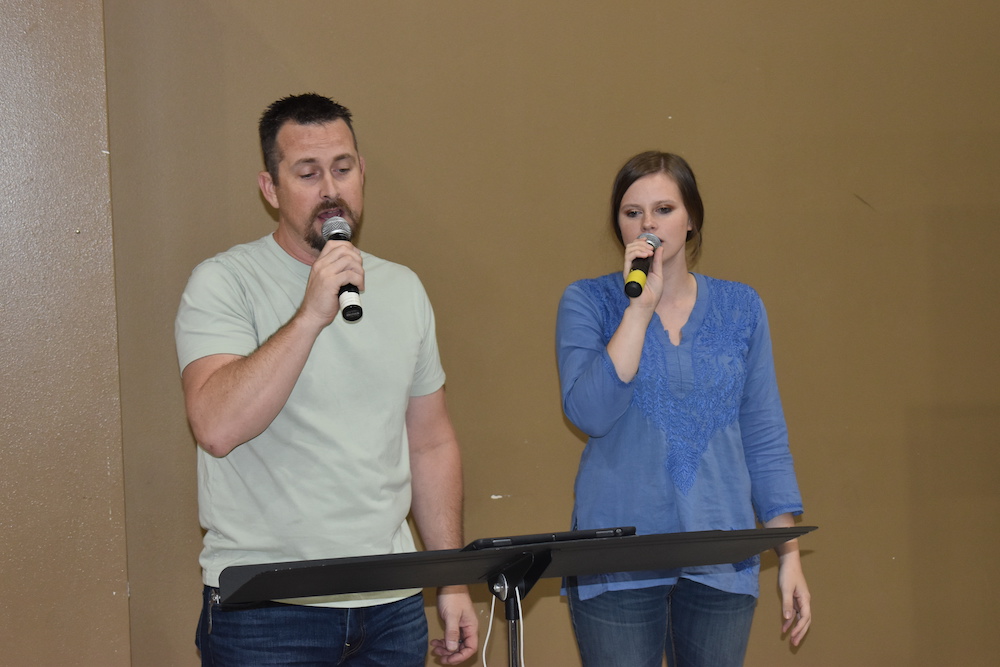 Two people are singing into microphones in front of a microphone stand.